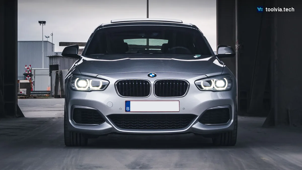 Silver BMW 1 Series hatchback with its headlights on, parked under a steel structure